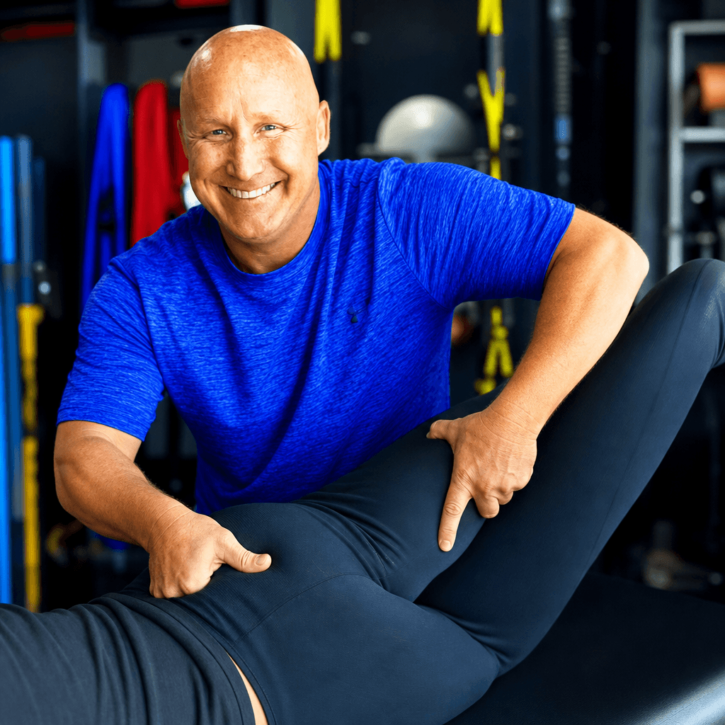 Smiling physical therapist in a blue shirt performs manual hip stretching on a client.